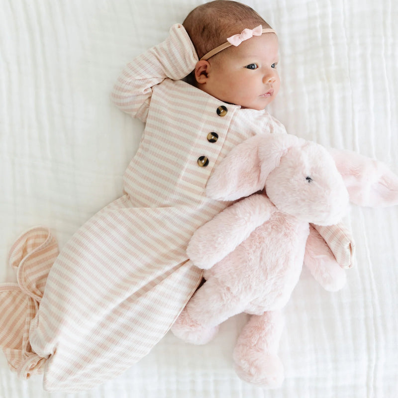 Baby in a striped outfit holding a pink plush toy on a white background