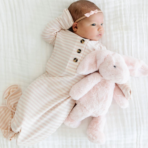 Baby in a striped outfit holding a pink plush toy on a white background