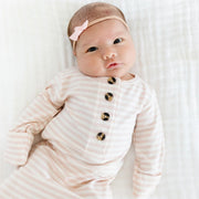 Baby wearing a striped outfit with buttons and a pink headband on a white background