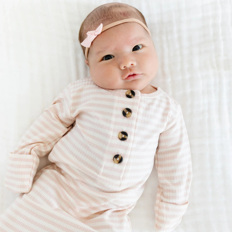 Baby wearing a striped outfit with buttons and a pink headband on a white background