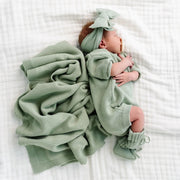 Newborn baby wrapped in a green blanket and outfit on a white surface