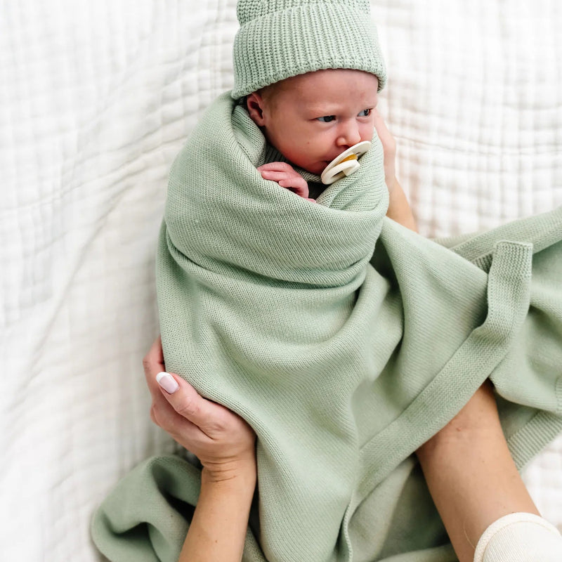 Newborn baby wrapped in a green blanket and hat on a white background