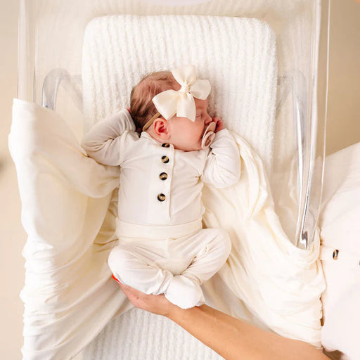 Baby in a white outfit with a bow in a clear crib