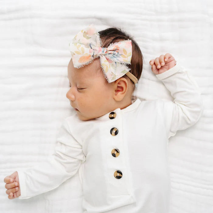 Newborn baby wearing a white outfit with buttons and a floral headband on a white background
