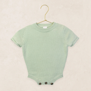 Green baby romper on a hanger against a beige background