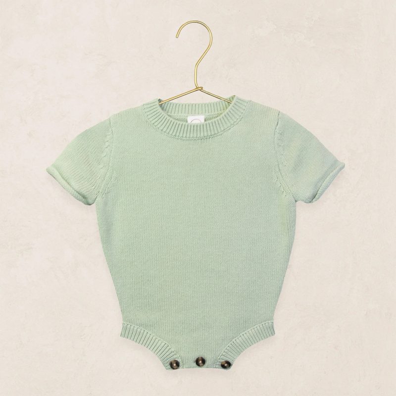 Green baby romper on a hanger against a beige background