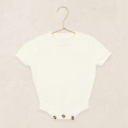Ivory baby onesie on a gold hanger against a beige background