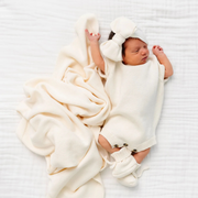 Newborn baby wrapped in a cream knit blanket and outfit on a white background