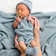 Newborn baby in light blue outfit with pacifier held by a person against a soft gray background