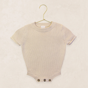 Tan baby romper on a hanger against a beige background