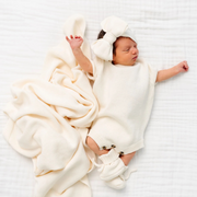 Newborn baby wrapped in a white blanket and wearing a matching hat on a white background