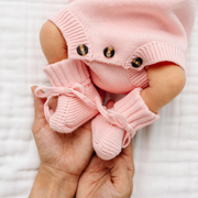 Pink knitted baby booties held by a hand against a white background