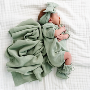 Newborn baby wrapped in a green knitted outfit and blanket on a white surface
