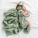 Newborn baby wrapped in a green knitted outfit and blanket on a white surface