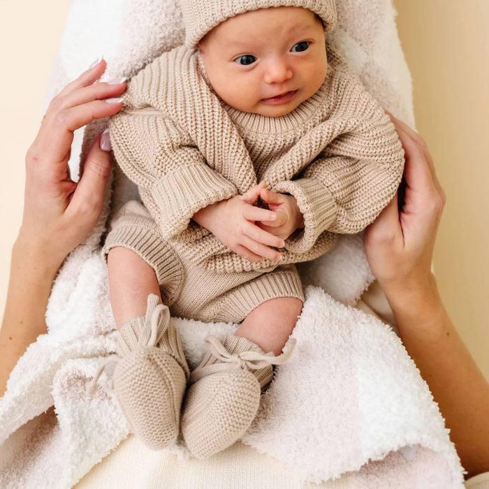 Newborn baby in beige knitted outfit being held on a white blanket