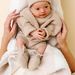 Newborn baby in beige knitted outfit being held on a white blanket