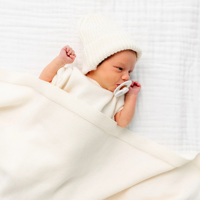 Newborn baby wrapped in a white blanket with a white hat on a white background