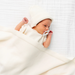 Newborn baby wrapped in a white blanket with a white hat on a white background