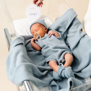 Newborn baby wrapped in a blue blanket with a pacifier, wearing a matching hat, in a crib.