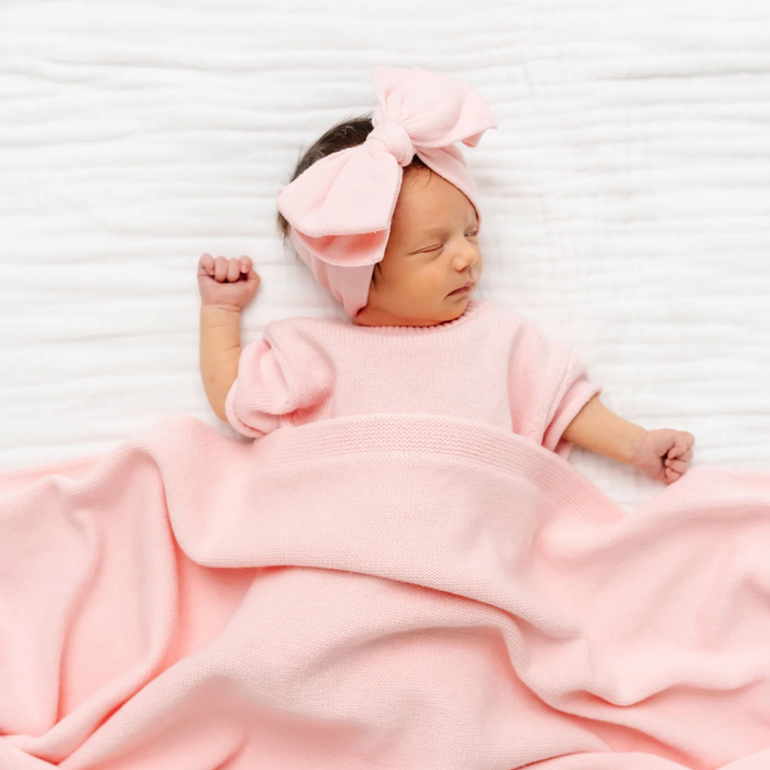 Newborn baby wrapped in a pink blanket and headband on a white background