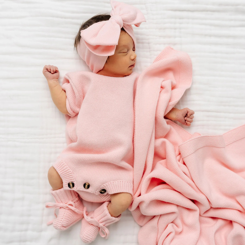 Newborn baby wrapped in a pink blanket and wearing a matching headband on a white background