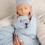 Newborn baby wrapped in a light blue blanket with a matching hat, held by a person.