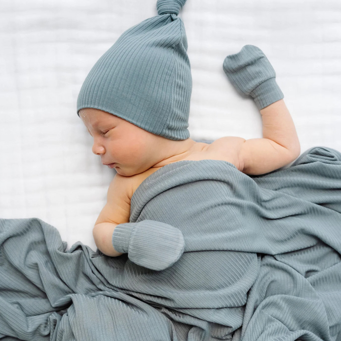 Newborn baby wrapped in a blue blanket and wearing a matching blue hat and socks on a white background
