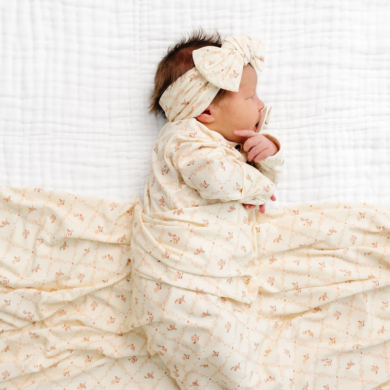 Newborn baby wearing Lou Lou & Co Annie floral gown and matching headband lying on white blanket