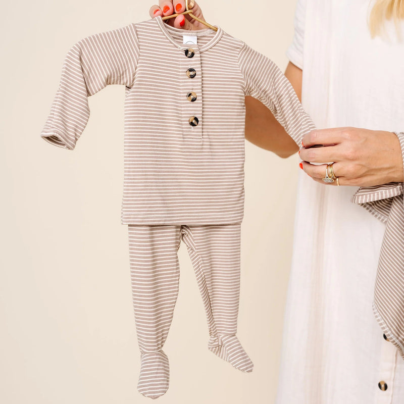 Lou Lou & Co Banks newborn striped top and bottom set in beige and white being held on hanger by adult in neutral outfit