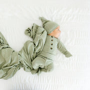 Newborn baby in Lou Lou & Co Carson striped outfit with matching knotted hat and blanket spread on a white bed