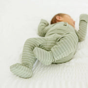 Newborn baby wearing Lou Lou & Co Carson green striped top and bottom set with built-in footies lying on a white bed