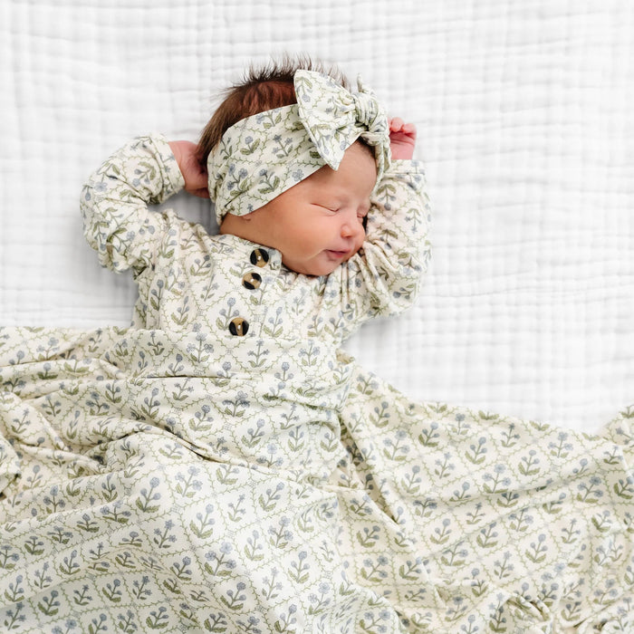 Close-up of Lou Lou & Co Etta fabric showing delicate blue flowers and green leaves in a repeating vine pattern on a creamy white background