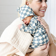 Newborn baby in Lou Lou & Co Miles checkered print outfit with matching hat being held by mother in cream clothing