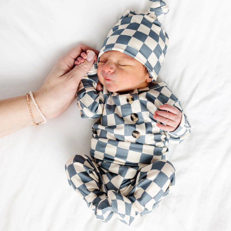 Newborn baby lying on white blanket wearing Lou Lou & Co Miles checkered top and bottom set with matching knotted hat