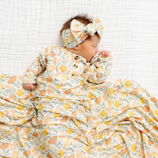 Newborn baby wearing Lou Lou & Co Phoebe floral gown and matching headband lying on a white quilted blanket