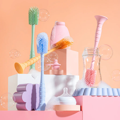 Collection of baby cleaning tools including brushes and sponges on a pastel pink background.