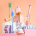 Collection of baby cleaning tools including brushes and sponges on a pastel pink background.
