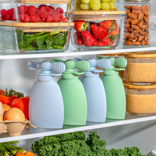 Four silicone food storage bags on a shelf with fresh produce in the background