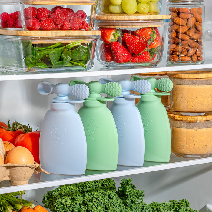 Four silicone food storage bags on a shelf with fresh produce in the background