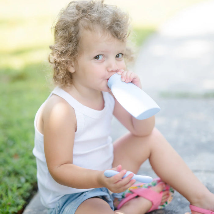 Child sitting outdoors drinking from a silicone feeding pouch