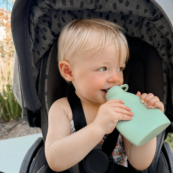 Child in a stroller holding a green silicone feeder cup outdoors