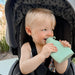 Child in a stroller holding a green silicone feeder cup outdoors