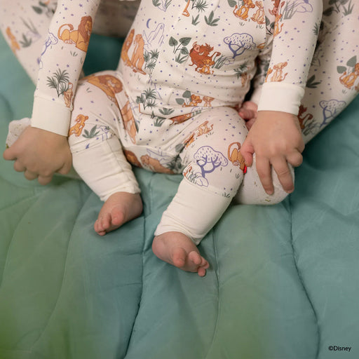 Baby in a onesie with animal prints sitting on a teal surface.