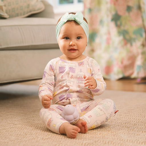 Baby sitting on a carpeted floor wearing a patterned outfit and headband, holding a toy.