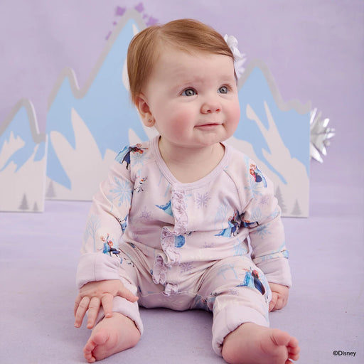 Baby wearing a onesie with character prints against a Disney-themed backdrop