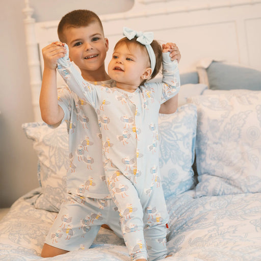 Two children in matching pajamas sitting on a bed.