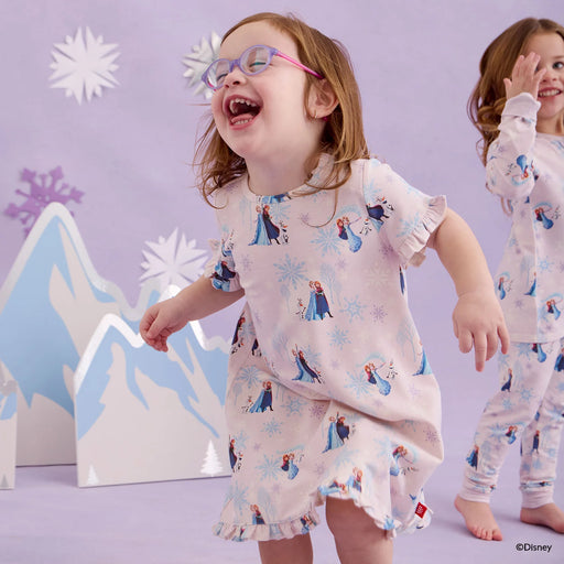 Two children wearing Frozen-themed pajamas in a snowy landscape setting.