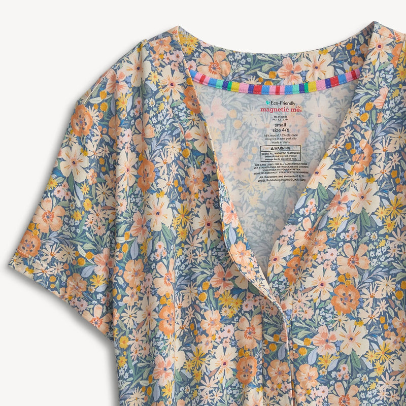 A close-up of a short-sleeve button-front top with a blue floral print, featuring white, peach, and yellow flowers with green leaves. The inner collar is decorated with a colorful striped band, and the inside label shows the brand 'You're Welcome'.