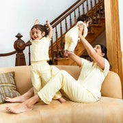 Woman and two children in matching light yellow outfits on a beige couch with a staircase in the background.