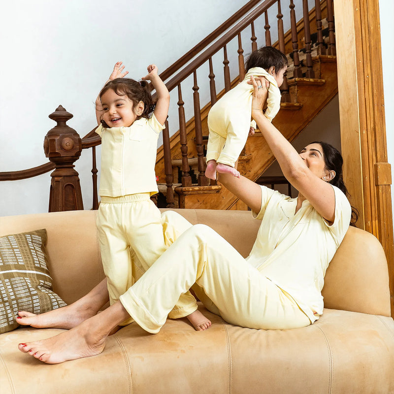 Woman and two children in matching light yellow outfits on a beige couch with a staircase in the background.